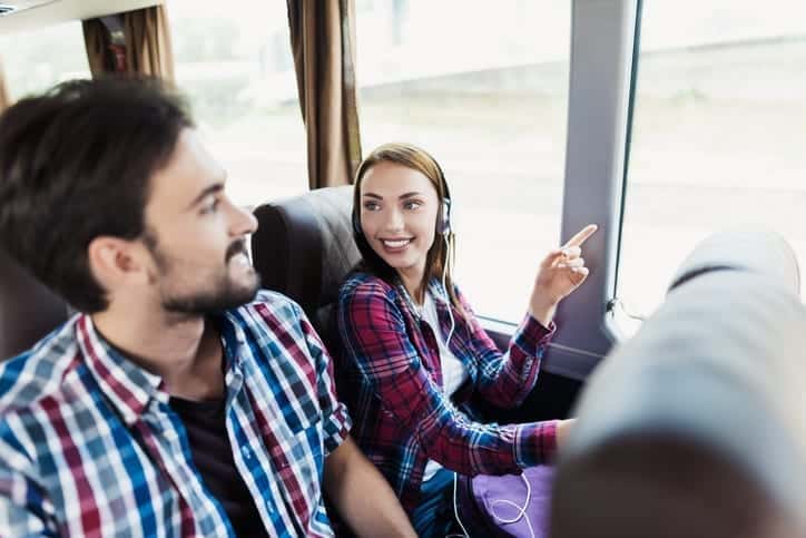 Charter Bus to Washington DC - Leprechaun Lines - The guy and the girl are on the bus. The girl has headphones. He and the guy are discussing something and smiling. Behind them sit other tourists who are looking out the window to the sights.